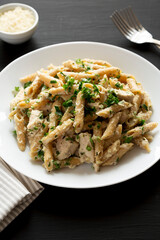 Homemade Chicken Alfredo Penne with Parsley on a black background, side view.