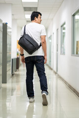 A man carry a black color strap bag on rear in office.