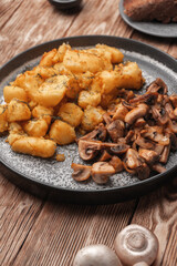 Fried potatoes with mushrooms on a gray plate next to fresh mushrooms