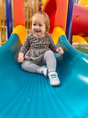 Fototapeta na wymiar Little happy girl with red hair in the park ride a slide