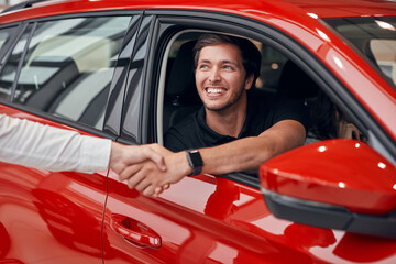 Happy male driver in car shaking hand with dealer
