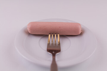 raw sausage with fork on white plate on white background