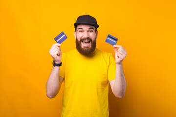 An excited young man is holding two credit cards looking at the camera .