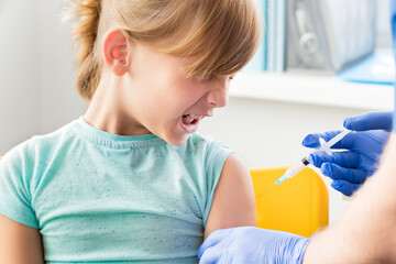 Little girl in face mask in doctor's office is vaccinated.Crying, scared, afraid of syringe with vaccine for covid-19 coronavirus,flu,infectious diseases.Clinical trials of injection for human, child