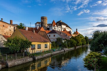 Fototapeta na wymiar Jindrichuv Hradec, Czech Republic - September 26 2019: View of the castle, the stone tower and historical buildings over the river Nezarka with reflection in water. Sunny day with blue sky and clouds.
