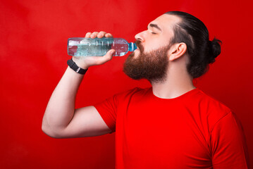 Photo of a bearded man drinking water from a glass bottle .