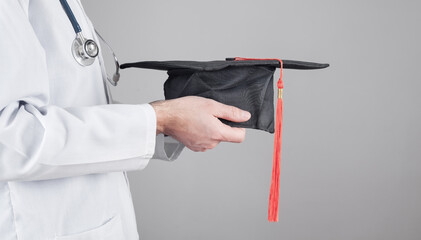 Caucasian doctor holding graduation hat. Medical education
