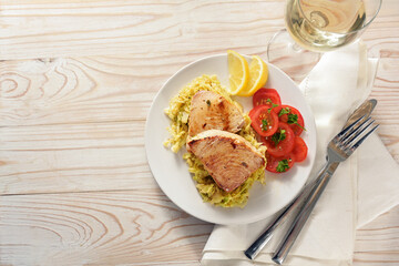 Fried tuna steaks on savoy cabbage, tomatoes and lemon served with wine on a plate and a white painted wooden table with napkin and cutlery, copy space, high angle view from directly above