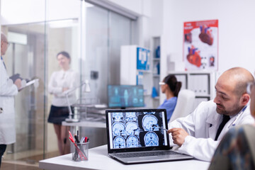 Woman speaking with doctor during consultation about cerebral x-ray using laptop in hospital. Senior patient visiting physician telling health complaints, medical practitioner explaining treatment.