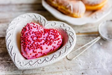 Donut with pink icing in the shape of a heart. Sweet Valentine's Day.