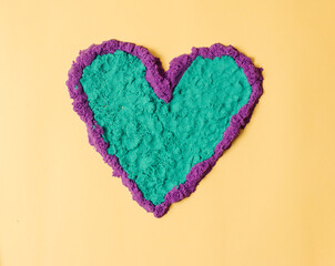 Green heart made of kinetic sand on yellow background