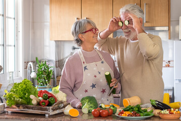 Vegetarian lifestyle. Beautiful elderly couple white-haired joke laughing in the kitchen with two slices of pumpkin. On the table a mix the of raw seasonal vegetables
