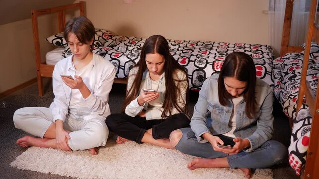 Spend time in social media via smartphone three triplet sisters teenager girls at home sit on floor in bedroom