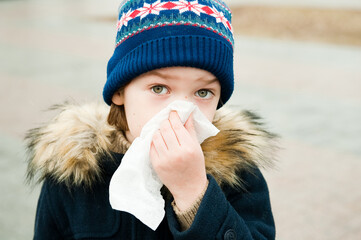 The child blows his nose in a handkerchief outside.