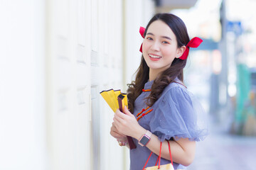 A young Asian woman in a blue-gray cheongsam holds a cloth bag next to a white wooden door with a city background. © nut_foto