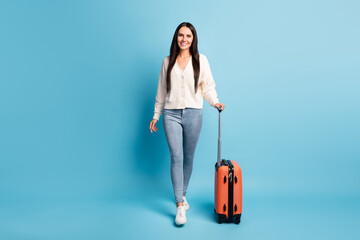 Full size photo of charming positive lady walking hand hold suitcase toothy smile isolated on blue color background