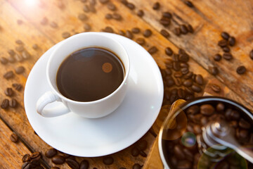 Coffee in a white cup and the grinding coffee beans place on the old wooden table. Aromatic morning coffee.