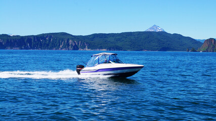 the boat goes through the water area of ​​Tikhaya Bay in Avachinsky Bay, in the background there are hills and the top of Vilyuchinsky volcano