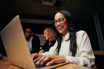 Close-up of successful smiling young African American businesswoman sitting near coworkers using laptop in office