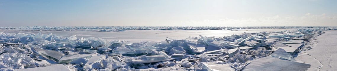 Panoramic view of the ice hummock field on the frozen Lake Baikal. Piles of snow-covered debris of blue ice on a sunny frosty day. Winter landscape. Harsh climate, cold weather. Natural background