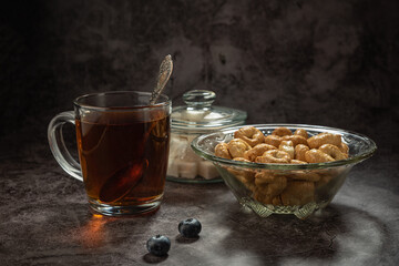 Tarallini in a glass bowl, with a glass cup of tea, and with a glass sugar bowl, blueberries on a gray mottled background
