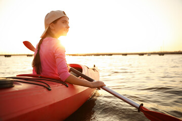 Happy girl kayaking on river at sunset. Summer camp activity