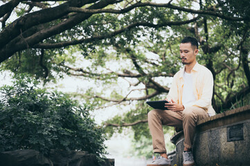 A young asian man chilling and relaxing by listen to music with headphone in the park. Good feeling of the sunny day at the garden in the vacation leisure time.