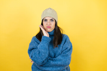 Young beautiful woman wearing blue casual sweater and wool hat thinking looking tired and bored with crossed arms