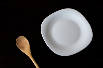 white plate and wooden spoon on black background