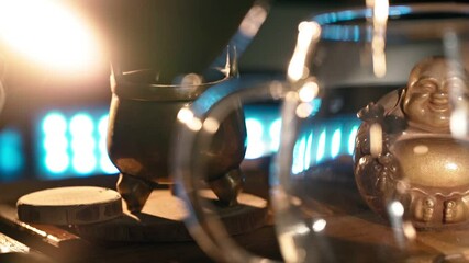 Black Hot Tea Poured into Beautiful Glass against background of the Smoke Coming from Scented Sticks, backlit by Warm Light. Tea ceremony. Oriental Cup close up. Unrecognizable person. Slow motion