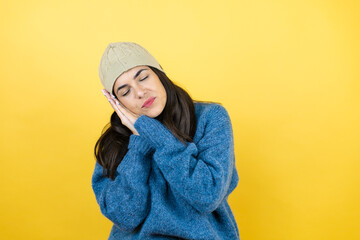 Young beautiful woman wearing blue casual sweater and wool hat sleeping tired dreaming and posing with hands together while smiling with closed eyes.