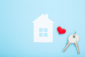 White paper house with bright red heart and two metal door keys on light blue table background....