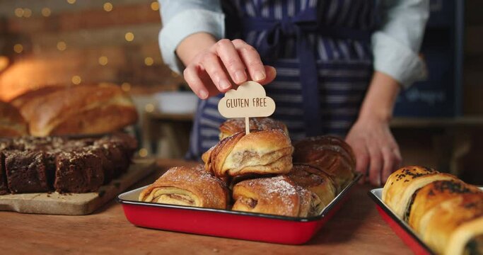 Sales Assistant In Bakery Putting Gluten Free Label Into Stack Of Freshly Baked Baked Cinnamon Buns