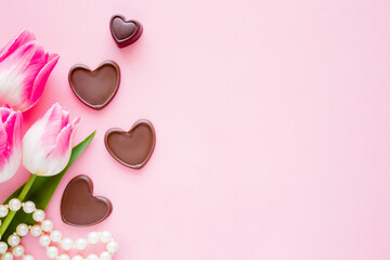 Tulips with brown black chocolate hearts and white beads on light pink table background. Pastel...