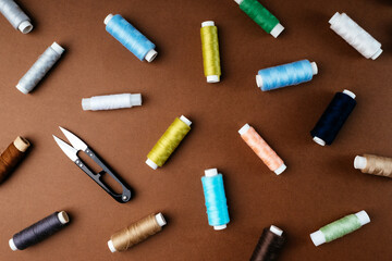 Composition of spools of thread and other sewing accessories on a brown background, flat flat, top view. Sewing accessories. Background for needlework, tailoring, atelier, clothing repair shop