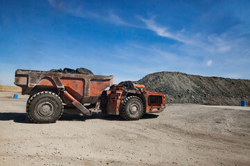 Orange heavy mine truck with ore. On empty stones and blue sky background.