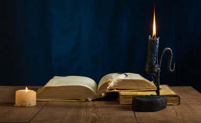 An old open book with a bird's feather lying on the second closed book and a candle holder made of...