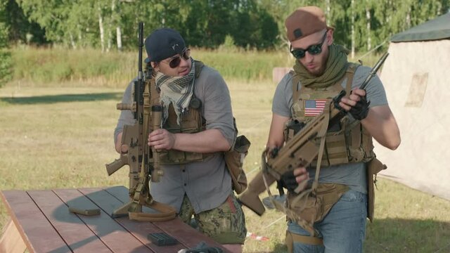 Medium footage of US military men practicing weapon assembling outdoors, fastening rifle suppressor to its main part
