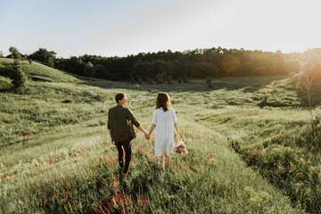 Young beautiful woman and man hug, kiss and walk in nature at sunset.