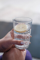 A glass with lemon water in hand close-up.