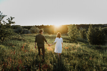 Young beautiful woman and man hug, kiss and walk in nature at sunset.