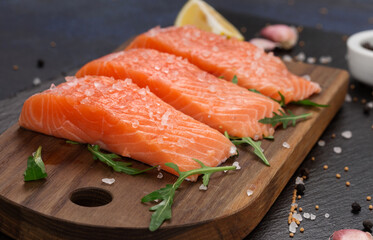 Raw fillet of salmon with sea salt, lemon and pepper on black stone background.