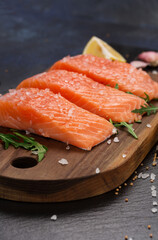 Raw fillet of salmon with sea salt, lemon and pepper on black stone background.