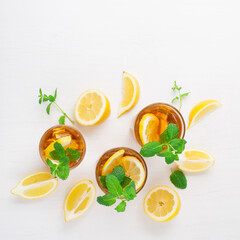 Iced tea with lemon slices, mint and ice on white wooden table, top view.