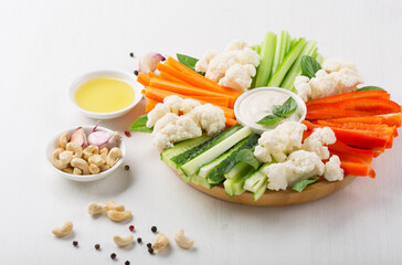 Carrot and cucumber sticks, pieces pepper with Vegan cashew cream sauce on white wooden background.