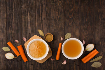 Traditional homemade beef bone broth with vegetable in glass jar on dark rustic wooden background.