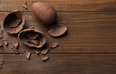 Broken chocolate eggs on wooden table, flat lay. Space for text