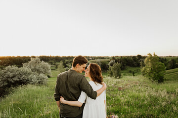 Young beautiful woman and man hug, kiss and walk in nature at sunset.