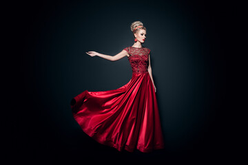 Fulll length image of a wonderful young woman dressd in a long fluing red dress with raised hand, over black background.