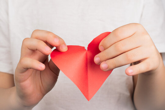 Blurred image of hands tearing a paper heart on a light background.